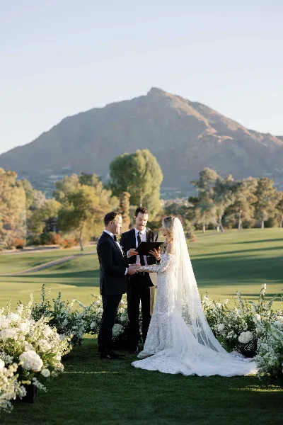 Bride and groom exchanging vows during an outdoor wedding ceremony on a golf course with a mountain in the background.