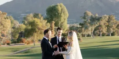 Bride and groom exchanging vows during an outdoor wedding ceremony on a golf course with a mountain in the background.