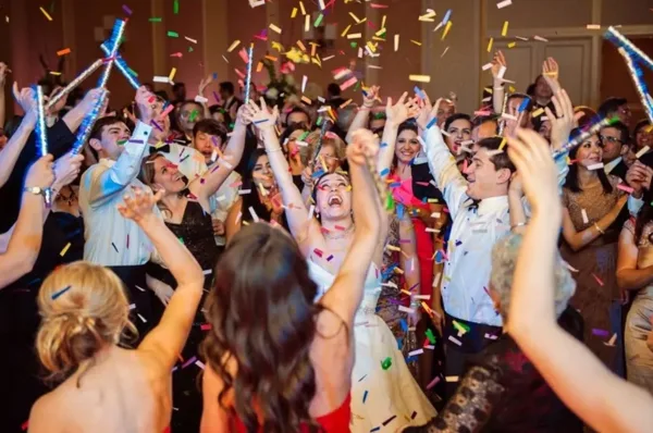 A bride and wedding guests dancing and celebrating with confetti at a reception.