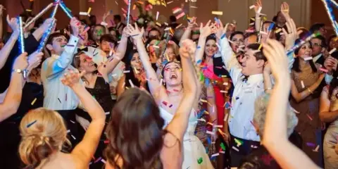 A bride and wedding guests dancing and celebrating with confetti at a reception.