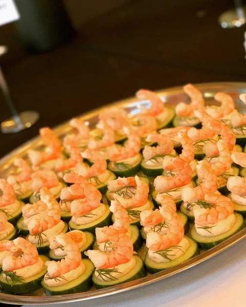 A silver serving tray filled with shrimp appetizers placed on cucumber slices with dill garnish.