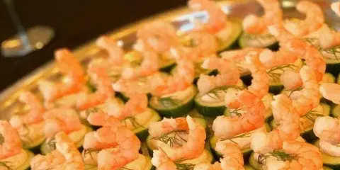 A silver serving tray filled with shrimp appetizers placed on cucumber slices with dill garnish.