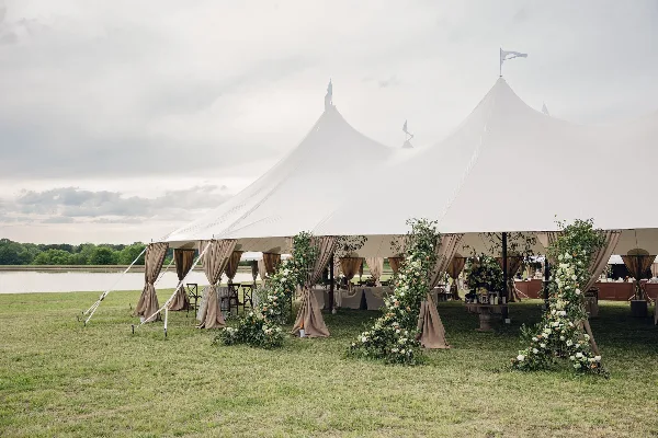 A large white event tent set up on a grassy field with beige draping and floral arrangements.