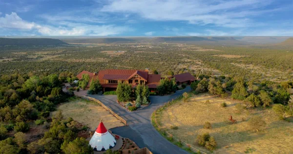 Aerial view of a large wooden lodge and tipi on a sprawling ranch property with a wide landscape background.