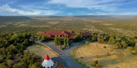 Aerial view of a large wooden lodge and tipi on a sprawling ranch property with a wide landscape background.