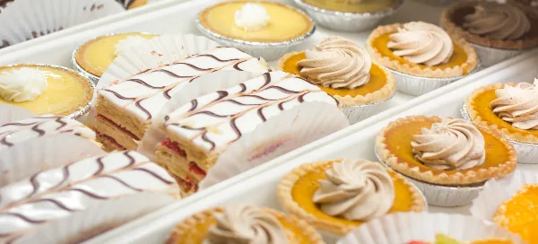 Trays of baked pastries including cream-filled slices with chocolate drizzle and small tarts topped with piped cream