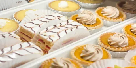 Trays of baked pastries including cream-filled slices with chocolate drizzle and small tarts topped with piped cream