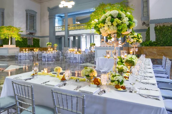 Wedding reception tables set with white linens, silver Chiavari chairs, glassware, flatware, and floral centerpieces in a ballroom.