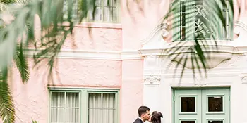 A bride and groom standing together in a courtyard with a pink building in the background.