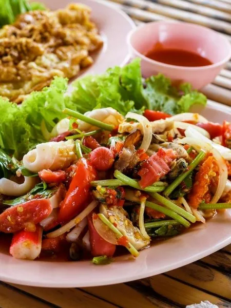 Plated seafood salad with lettuce, tomatoes, and a dipping sauce served on a table.