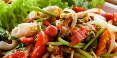 Plated seafood salad with lettuce, tomatoes, and a dipping sauce served on a table.