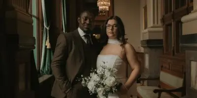 A professional wedding portrait of a couple standing in an elegant hallway with a chandelier.