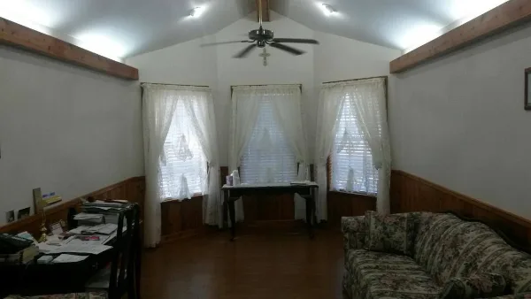 Interior view of an office or meeting room with a floral sofa, a desk with paperwork, and a ceiling fan.