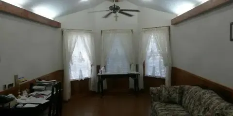 Interior view of an office or meeting room with a floral sofa, a desk with paperwork, and a ceiling fan.