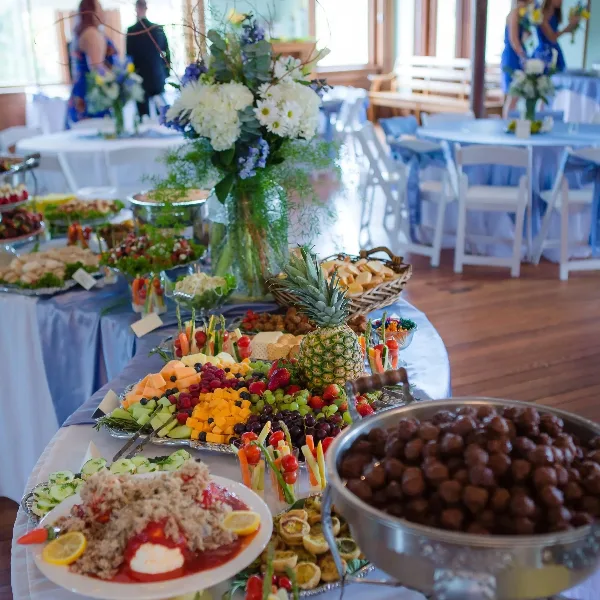 Catering buffet table with fruit platters, vegetable trays, and food bowls set up for an event.