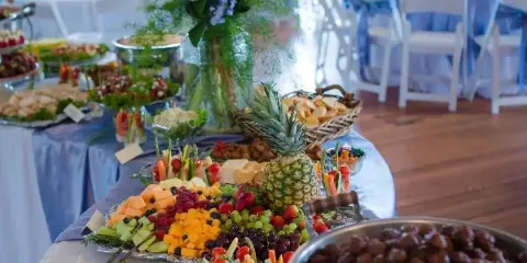 Catering buffet table with fruit platters, vegetable trays, and food bowls set up for an event.