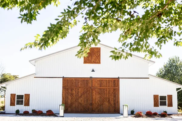 Exterior view of a white barn-style wedding venue with large wooden sliding doors and surrounding greenery.