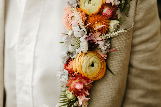 A close-up of a colorful floral boutonniere pinned to the lapel of a beige suit jacket.