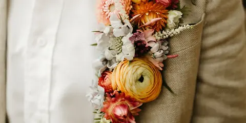 A close-up of a colorful floral boutonniere pinned to the lapel of a beige suit jacket.