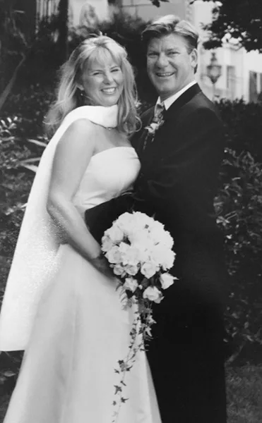 A black and white photograph of a bride and groom standing together, with the bride holding a bouquet of white flowers.