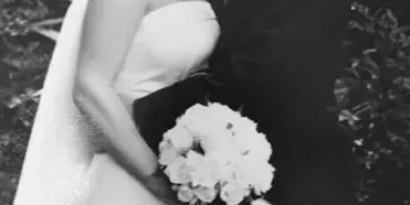 A black and white photograph of a bride and groom standing together, with the bride holding a bouquet of white flowers.