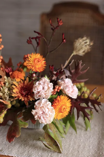 A close-up of a floral arrangement with orange chrysanthemums, pale pink roses, and dark foliage.