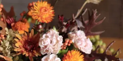 A close-up of a floral arrangement with orange chrysanthemums, pale pink roses, and dark foliage.