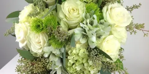 A lush floral arrangement with white roses, green chrysanthemums, and hydrangeas.
