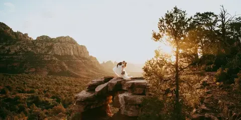 A bride and groom kissing on a rocky cliff overlooking a desert canyon at sunset.