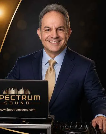 Portrait of a smiling man in a suit standing behind a DJ mixing console and laptop.