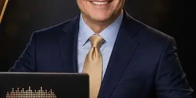 Portrait of a smiling man in a suit standing behind a DJ mixing console and laptop.