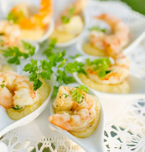 A close-up photograph of shrimp appetizers served in small white dishes, garnished with fresh parsley.