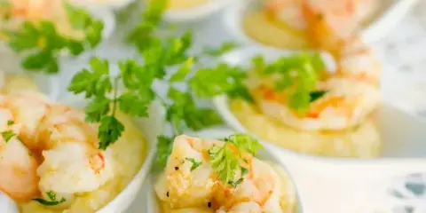 A close-up photograph of shrimp appetizers served in small white dishes, garnished with fresh parsley.