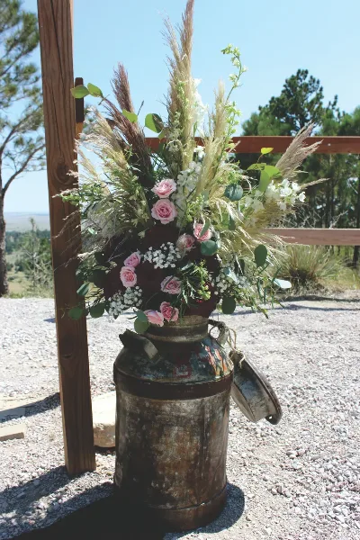 A rustic floral arrangement with pink roses and dried grasses in a vintage metal container.