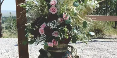 A rustic floral arrangement with pink roses and dried grasses in a vintage metal container.