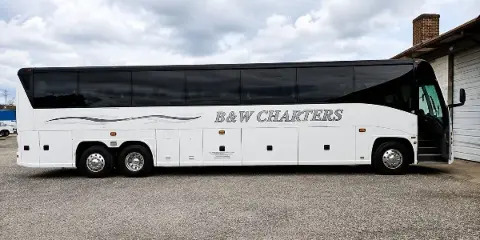 A white B&W Charters motorcoach bus parked on a gravel lot.