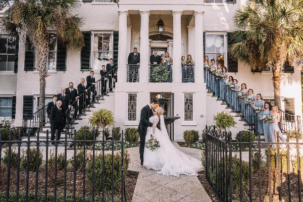 Wedding party posing on the exterior staircase and balcony of a historic white residence with columns.