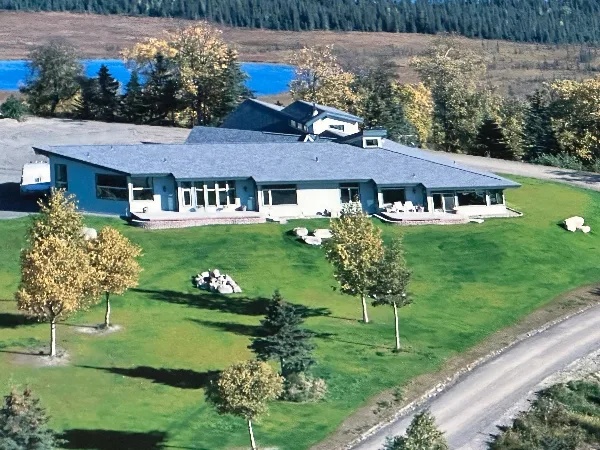Aerial view of a large private estate with a long building, expansive green lawn, and surrounding trees and water.