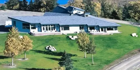 Aerial view of a large private estate with a long building, expansive green lawn, and surrounding trees and water.