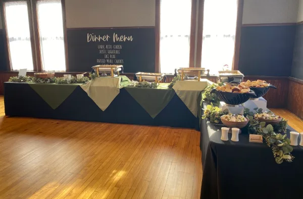 A catering buffet setup with a dinner menu board, food stations, and event decor in a venue.