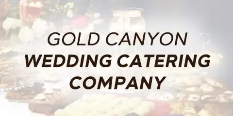 A catering buffet table with various food dishes and a floral arrangement.