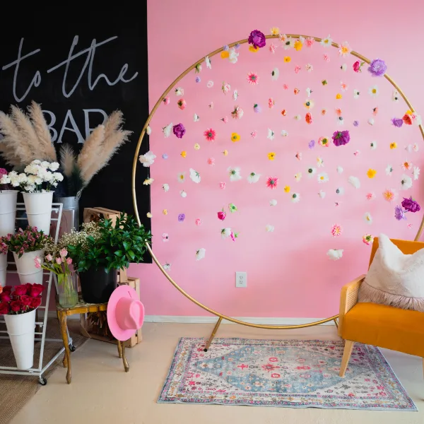 Interior of Fleur de Mer flower bar with a pink wall, gold hoop floral installation, and a mustard-colored chair.