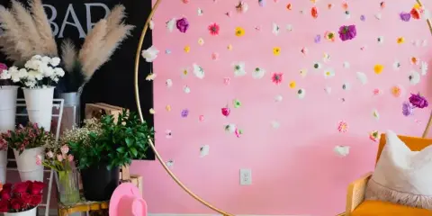 Interior of Fleur de Mer flower bar with a pink wall, gold hoop floral installation, and a mustard-colored chair.
