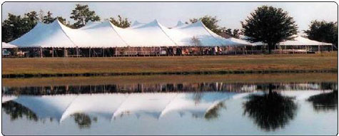 A large white event tent set up on a grassy field near a body of water.