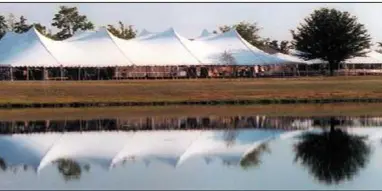 A large white event tent set up on a grassy field near a body of water.