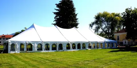 A large white event tent set up on a green lawn under a clear blue sky.