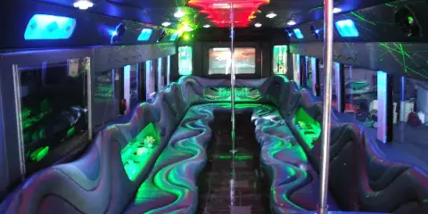 Interior of a party bus with a central dance pole, wet bar, and colorful party lighting.