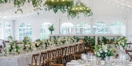 Elegant wedding reception interior with white tent ceiling, hanging greenery chandeliers, and floral table centerpieces.