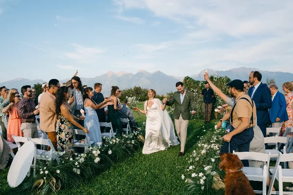 A bride and groom walking down the aisle at an outdoor wedding ceremony with guests on either side.