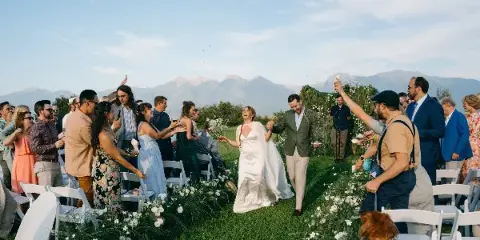A bride and groom walking down the aisle at an outdoor wedding ceremony with guests on either side.